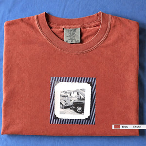 Brick folded t-shirt with vintage photo of mechanics and cars on front of shirt.