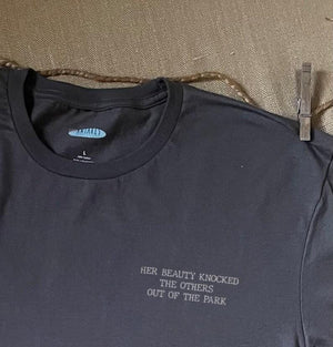 Close up shot of collage art t-shirt with tagline on front: 'Her Beauty Knocked The Others Out Of The Park'