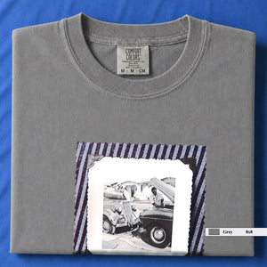 Folded light grey t-shirt with a large vintage photo of mechanics and cars on front of shirt.