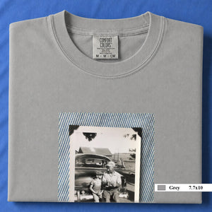 Grey colored folded t-shirt with a large vintage photo of a father and his son sitting on the bumper of an old car.