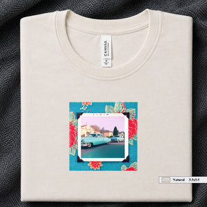 Ivory colored folded t-shirt with a vintage photo of two classic 50's cars on the street. Photo is surrounded by floral fabric.