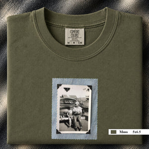 Moss colored folded t-shirt with a small vintage photo of a father and his son sitting on the bumper of an old car.