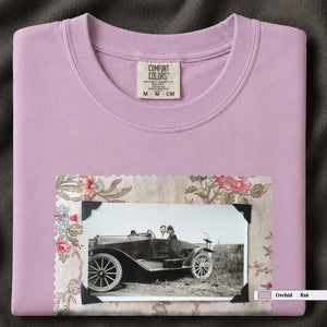 Orchid colored folded t-shirt with large vintage snapshot of people riding in a 1920's car surrounded by a floral design.