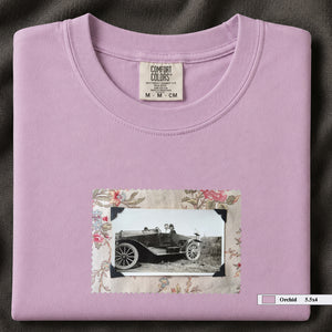 Orchid colored folded t-shirt with small vintage snapshot of people riding in a 1920's car surrounded by a floral design.