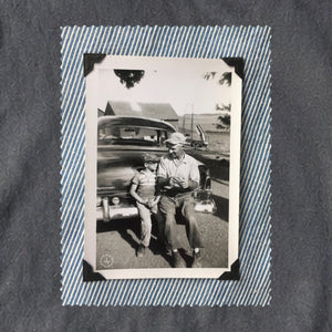 A vintage photo of a father and his son sitting on the bumper of an old car.