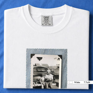 White colored folded t-shirt with a large vintage photo of a father and his son sitting on the bumper of an old car.