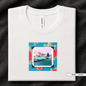 White colored folded t-shirt with a vintage photo of two classic 50's cars on the street. Photo is surrounded by floral fabric.
