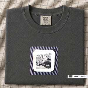 Charcoal colored folded t-shirt with vintage photo of mechanics and cars on front of shirt.