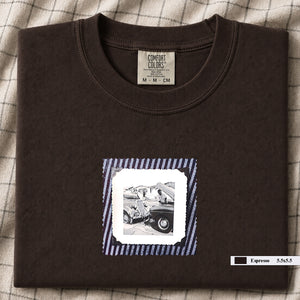 Dark brown colored folded t-shirt with vintage photo of mechanics and cars on front of shirt.