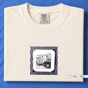 Ivory folded t-shirt with vintage photo of mechanics and cars on front of shirt.