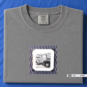 Light grey folded t-shirt with vintage photo of mechanics and cars on front of shirt.