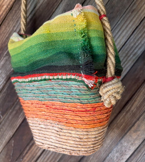 Back view of a handmade basket shoulder bag with a Mexican blanket textile and natural fiber floral detail.