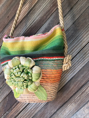 Front detail of a handmade basket shoulder bag with a Mexican blanket textile and natural fiber floral detail.