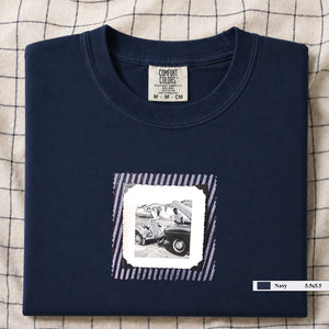Navy folded t-shirt with vintage photo of mechanics and cars on front of shirt.