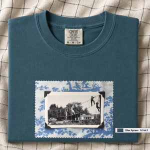 Teal colored folded tshirt with large vintage photo of kids playing in trees on front of shirt