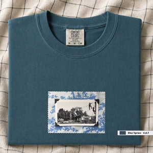 Teal colored folded tshirt with small vintage photo of kids playing in trees on front of shirt