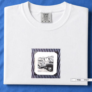White folded t-shirt with vintage photo of mechanics and cars on front of shirt.