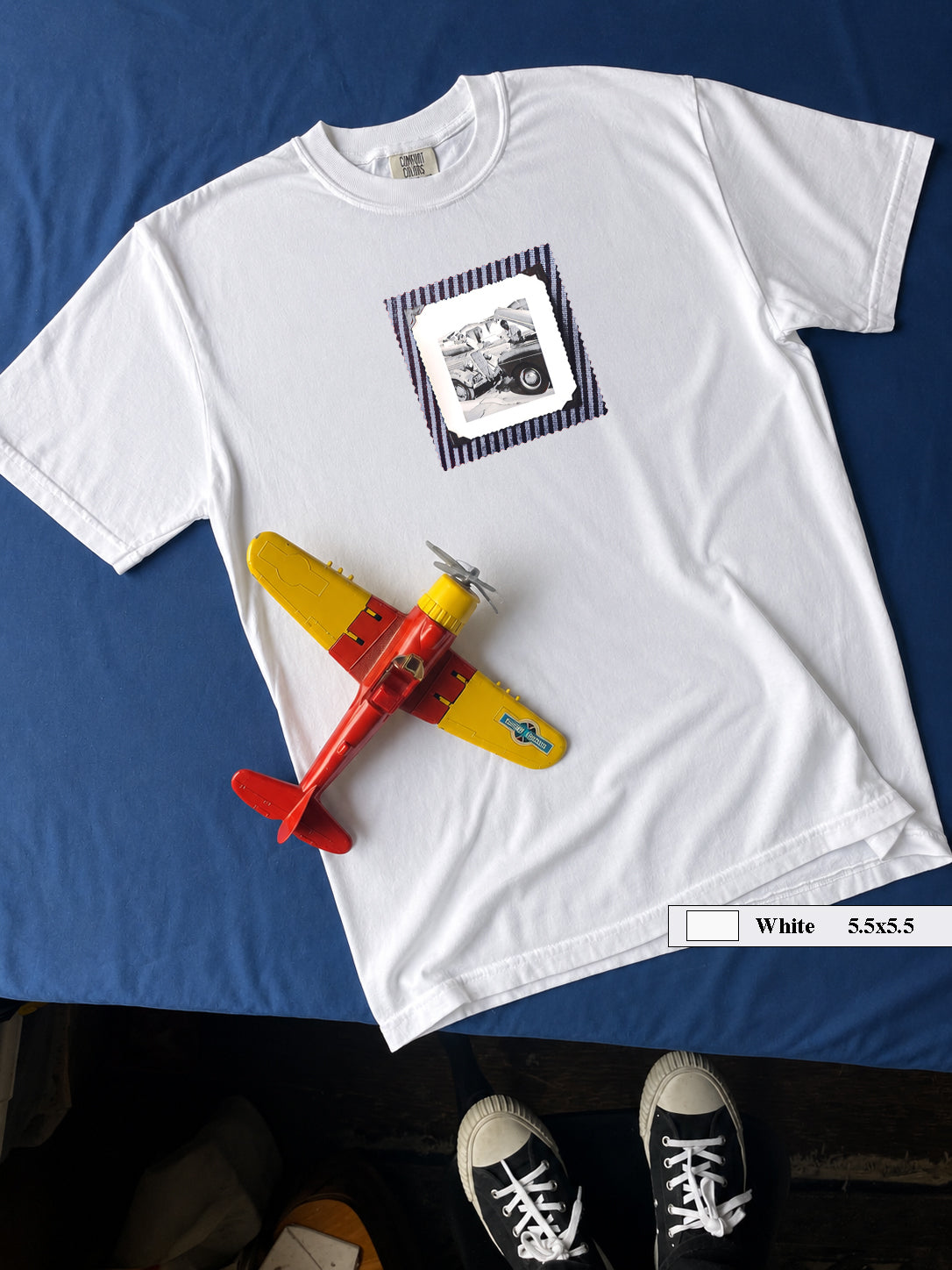 White t-shirt on table with vintage photo of mechanics and cars on front of shirt.